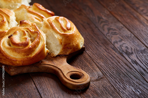 Homemade rose buns on wooden cutting board over rustic vintage background, close-up, shallow depth of field photo