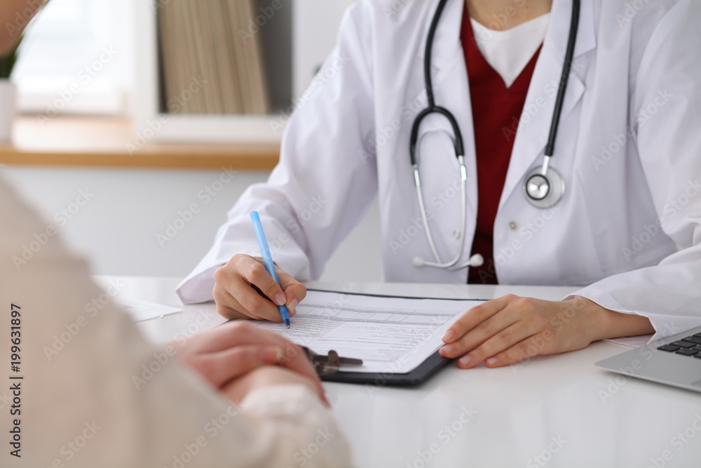 Close up of a female doctor filling up an application form while consulting patient Close up of a female doctor filling up an application form while consulting patient