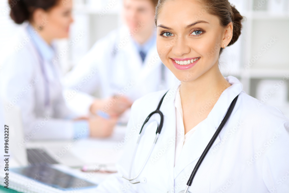 Happy female doctor keeping medical clipboard while medical staff are at the background Happy female doctor keeping medical clipboard while medical staff are at the background