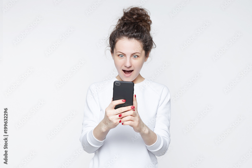 Excited happy stylish hipster lady reads news online, uses free internet connection on modern cell phone, finds out big sales. Surprised female model receives pleasant message about winning a prize. Excited happy stylish hipster lady reads news online, uses free internet connection on modern cell phone, finds out big sales. Surprised female model receives pleasant message about winning a prize.
