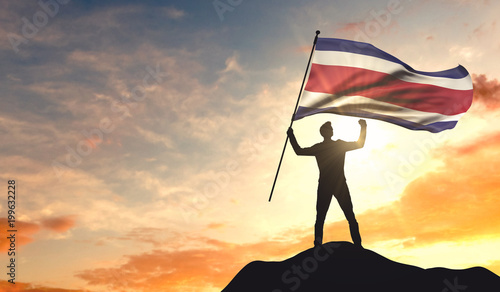 Costa Rica flag being waved by a man celebrating success at the top of a mountain. 3D Rendering photo