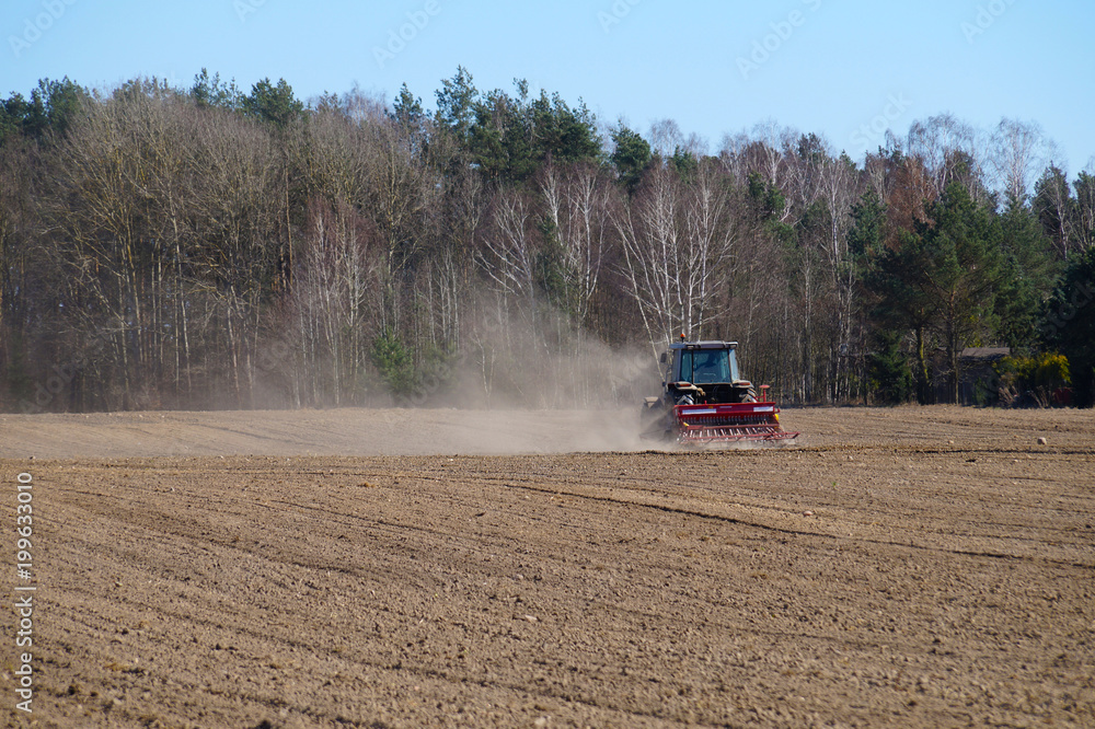 Fototapeta premium The tractor harrows fields for cultivation. Spring field work.