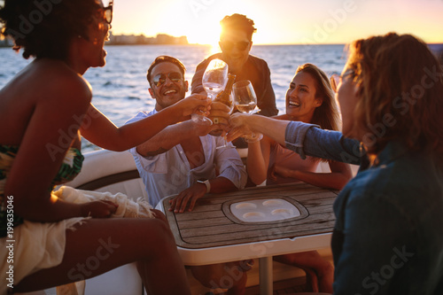 Group of friends having drinks at sunset boat party