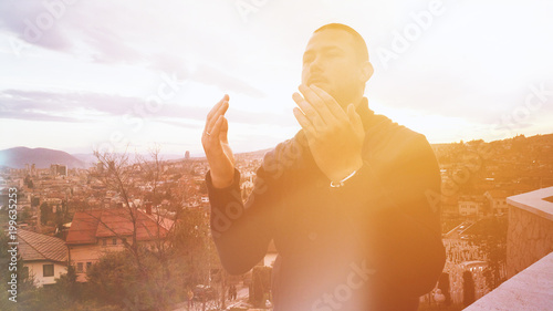 Young adult muslim man praying outdoor with hands up in the air