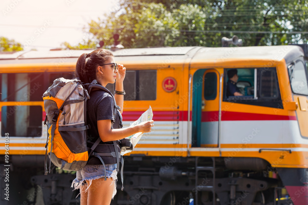 Obraz premium Young asian woman traveler with backpack and sunglass looking the map with train background at Ayutthaya train station.