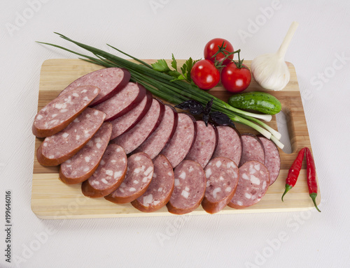 still life with sliced smoked sausage greens and tomatoes on a white background