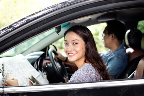 Asian woman using smartphone and map and men driving car on road trip and Happy young couple with a map in the car.