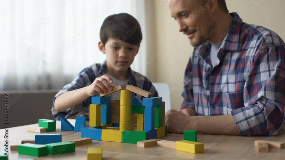 Caring daddy and his smiling son playing colored toy cubes at home, childhood Caring daddy and his smiling son playing colored toy cubes at home, childhood