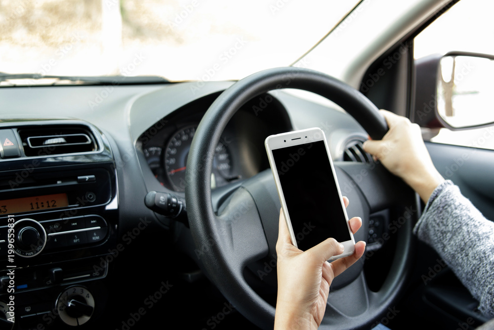 Woman hand holding mobile phone sending a text while driving a car. Selective focus.