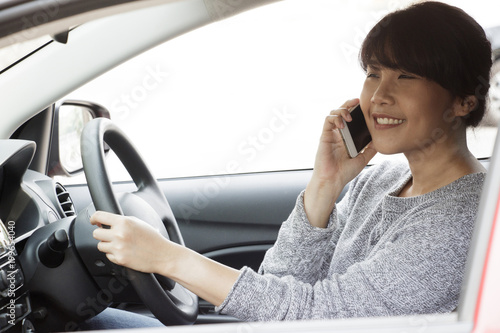 Young asian woman in casual wear driving a car, using smart phone and  looking on road. Risky driving. Woman sitting in car with cell phone © immstudio