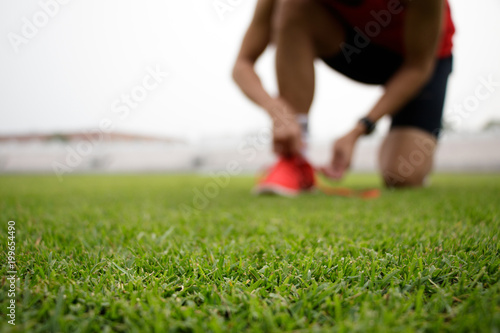 Man tying running shoes on the grass. Selective focus.