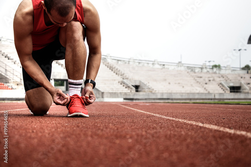 Young man runner tying shoelaces. Athletic man running on stadium track. Sport concept.