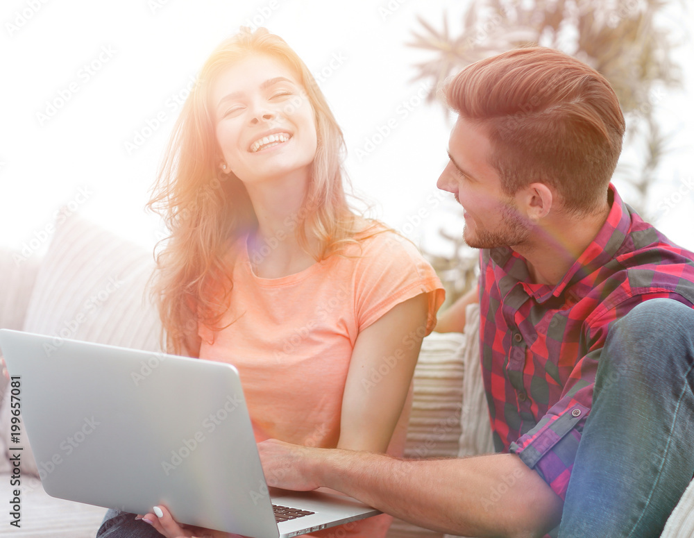 young couple is using a laptop and smiling while sitting on sofa at home young couple is using a laptop and smiling while sitting on sofa at home