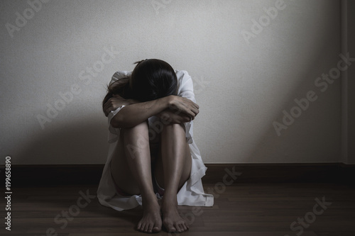 Depressed and stressed woman sitting on the floor alone head in hands in the dark room