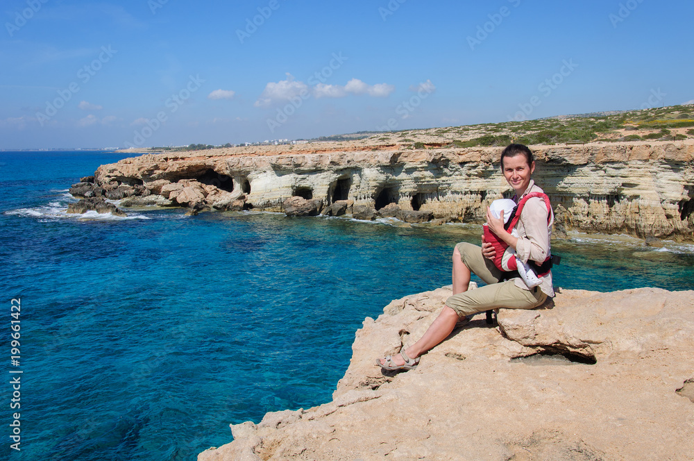 young woman with child sitting on stone precipice and looks at a storm on the Mediterranean Sea