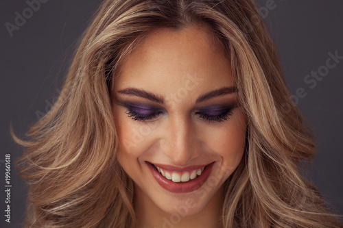 Lovely blonde woman smiling with eyes closed while wearing purple eyeshadow