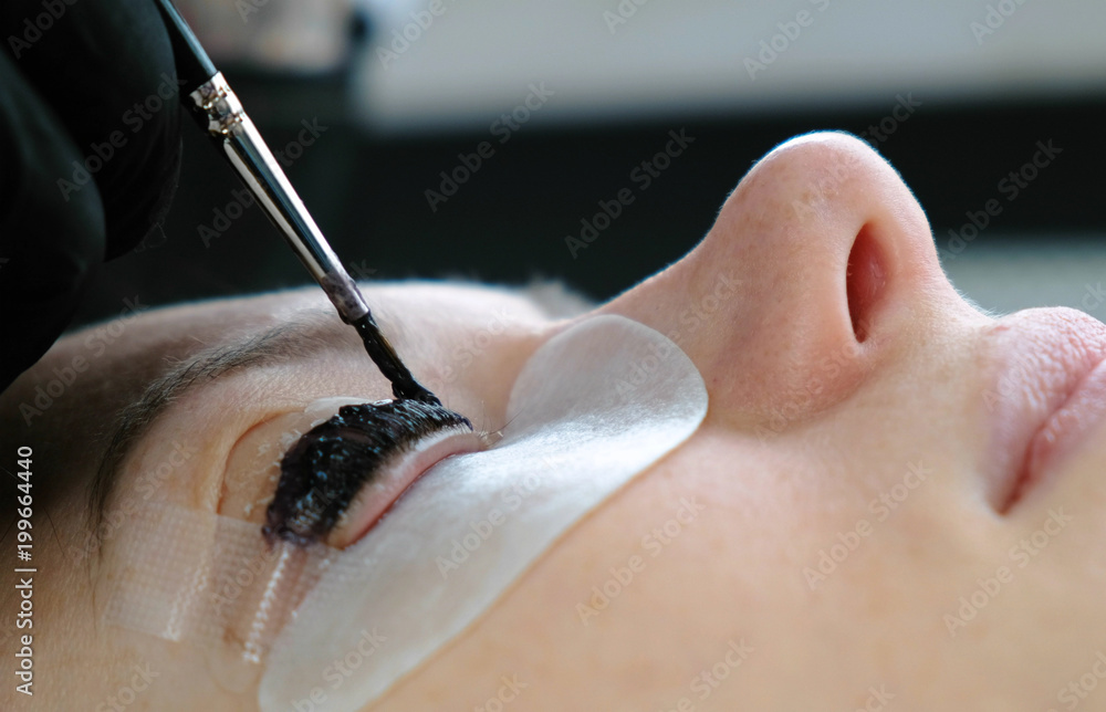 Fototapeta premium Beauty treatment. Cosmetologist puts black paint on the lashes. laminating eyelashes. Closeup face side view.