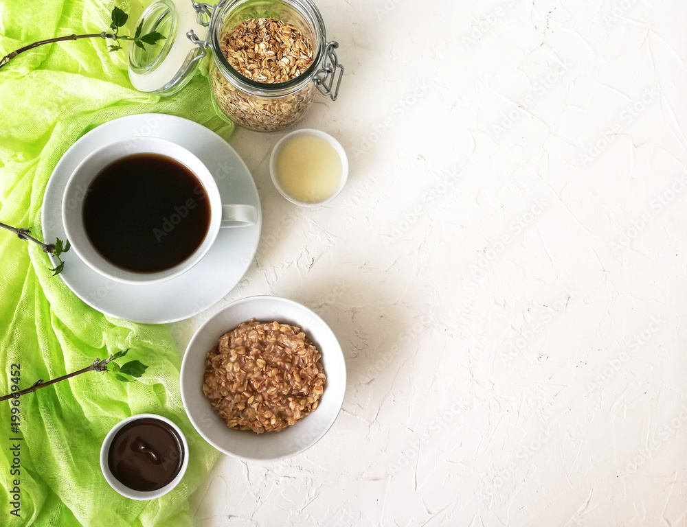 Breakfast with oatmeal in white bowl with coffee on wooden table, with light green runner and twigs of wood with green leaves Breakfast with oatmeal in white bowl with coffee on wooden table, with light green runner and twigs of wood with green leaves
