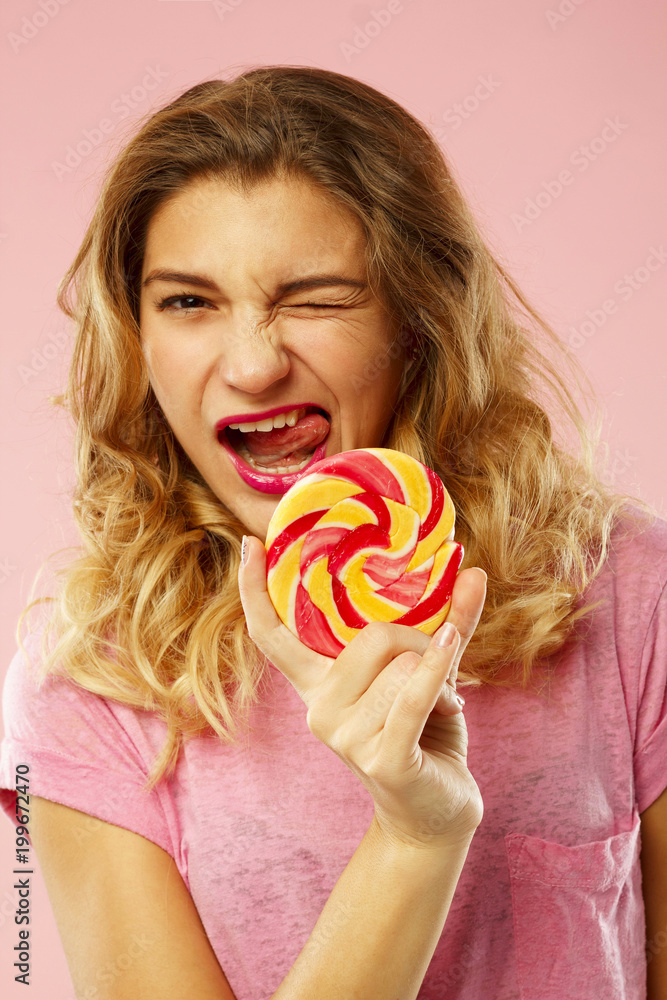 Portrait of a happy pretty girl holding sweet candy over pink background