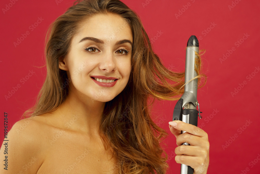 Young smiley woman making curly hair by ploy over red background Young smiley woman making curly hair by ploy over red background