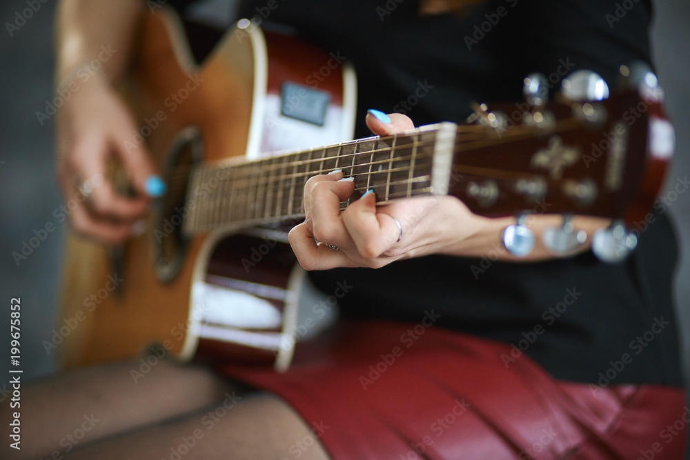 Fototapeta premium young girl in a red leather miniskirt and black pantyhose playing the guitar, close-up, shallow depth of field.