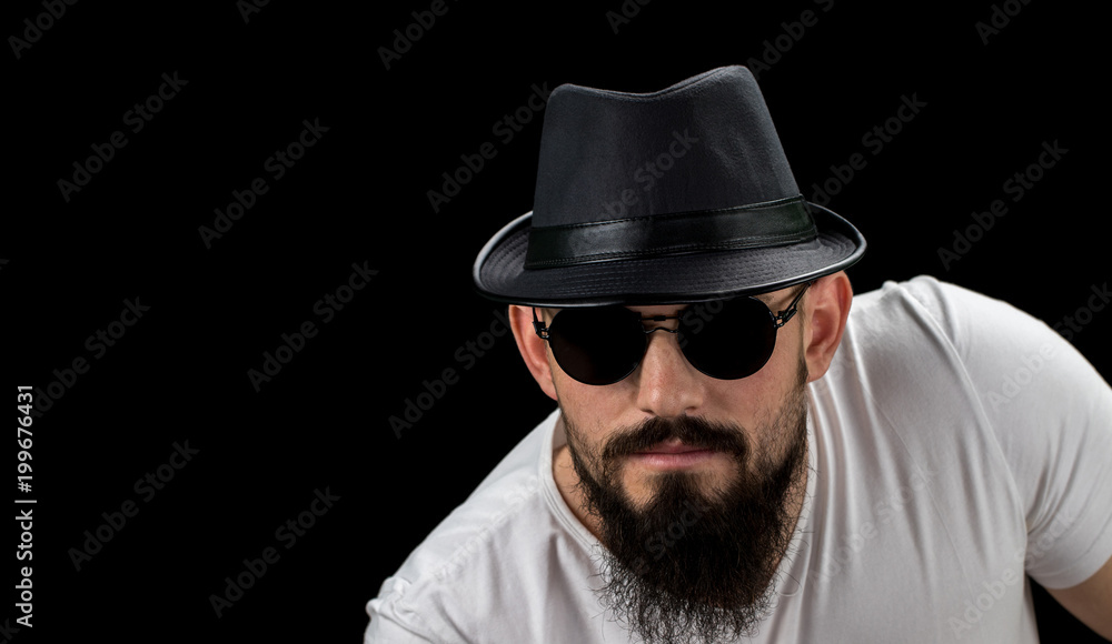 Silhouette of young confident handsome bearded man hipster in hat and sunglasses. Studio shot on dark background Image with free copy space