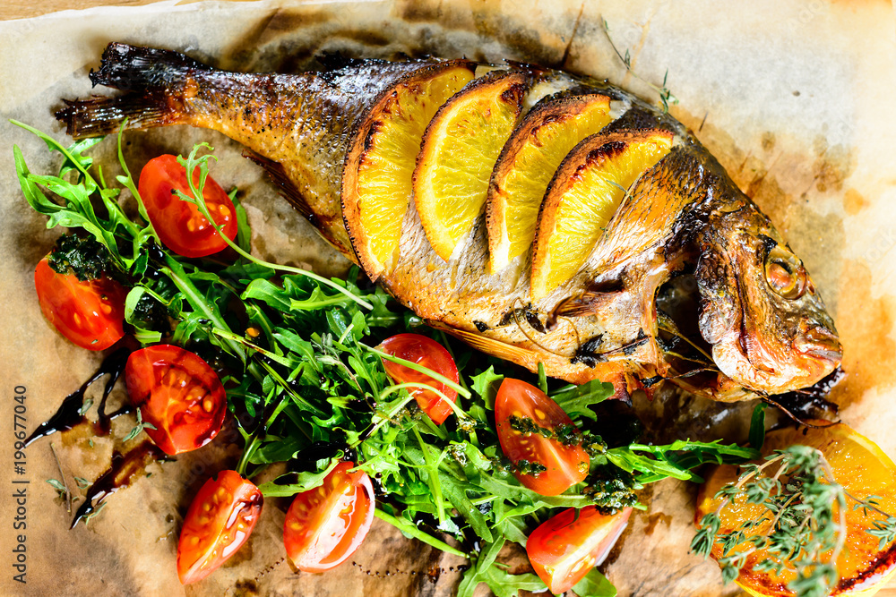 Delicious fish served with tomatoes, lemon and herbs on the wooden board. Top view, flat lay Delicious fish served with tomatoes, lemon and herbs on the wooden board. Top view, flat lay