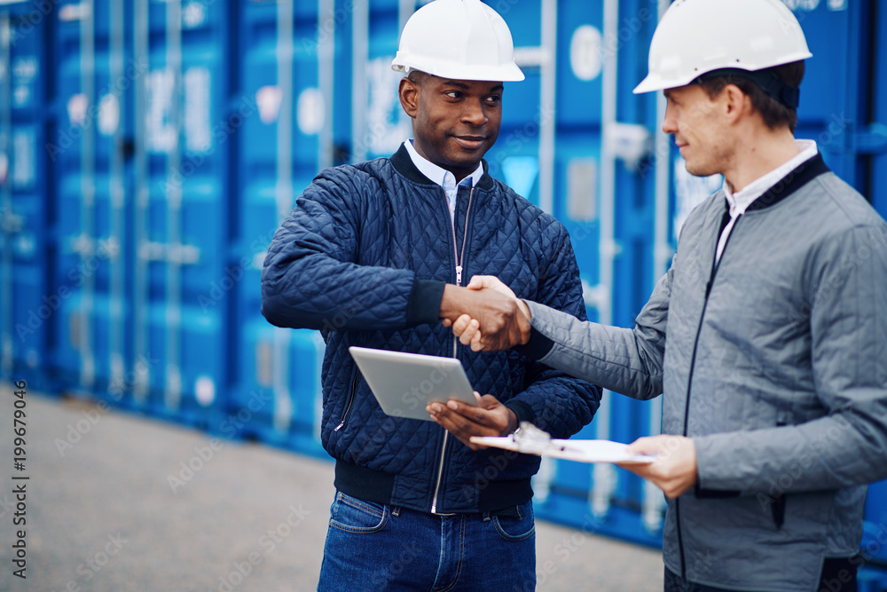 Engineers standing in a shipping yard shaking hands together Engineers standing in a shipping yard shaking hands together