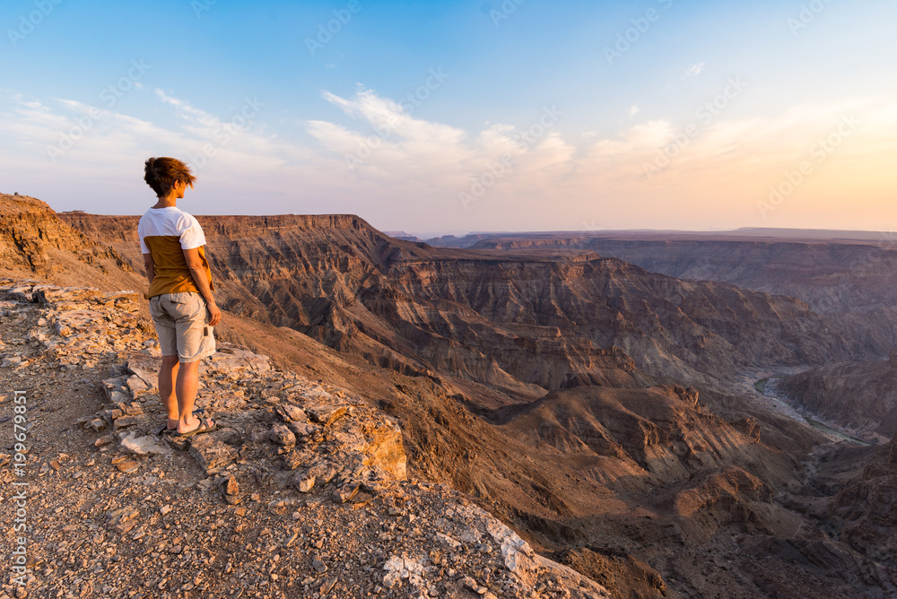 One person looking at the Fish River Canyon, scenic travel destination in Southern Namibia. Expansive view at sunset. Wanderlust traveling people.
