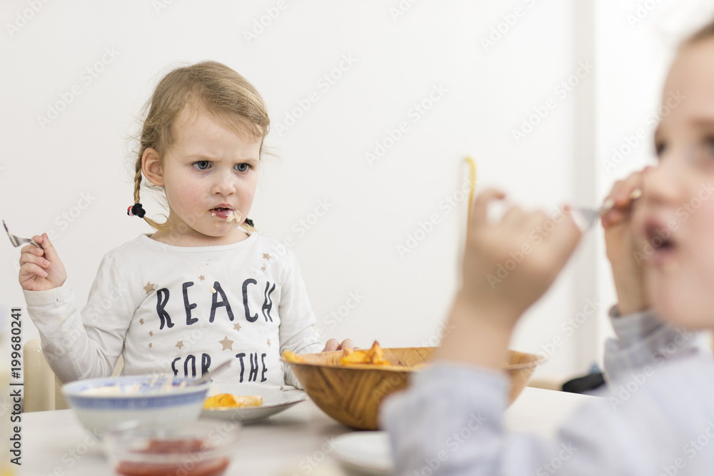 Little Kid Looking Annoyed at Her Sister While Eating Little Kid Looking Annoyed at Her Sister While Eating