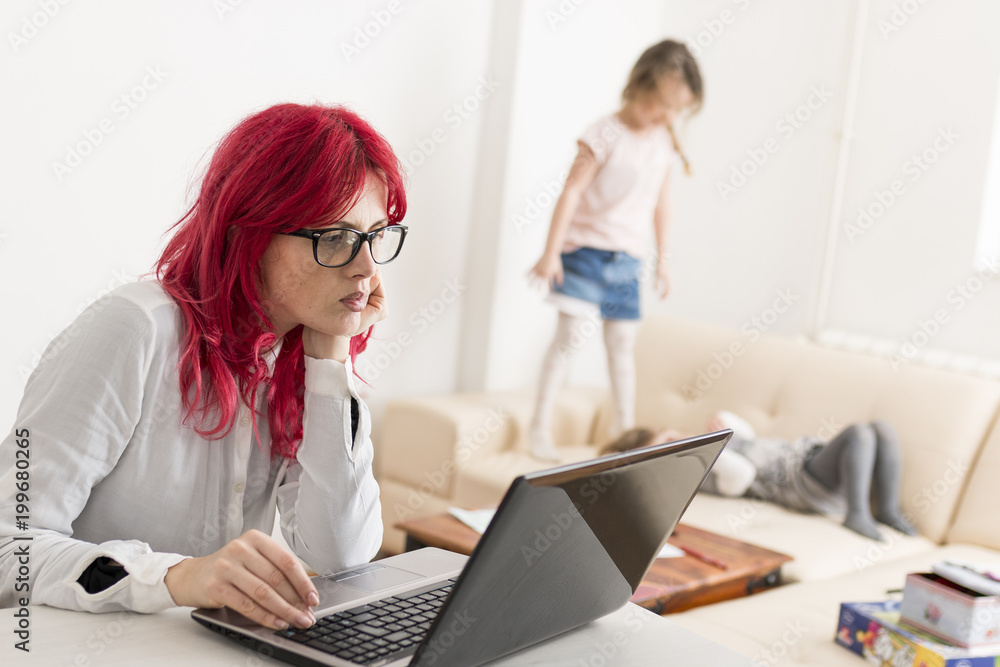Mother Using a Laptop Computer as Kids Play on Couch Mother Using a Laptop Computer as Kids Play on Couch