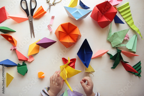 the child makes origami. Multicolored Origami and paper on  a white table. origami lesson photo
