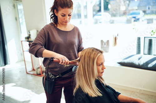 Young woman having her hair straightened by a hairdresser photo