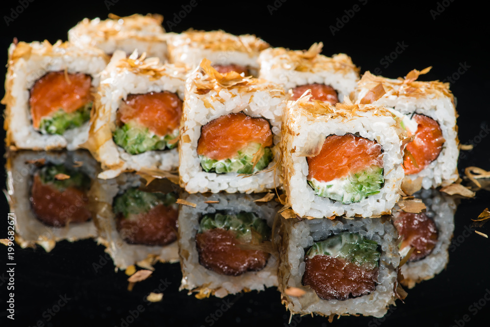 Traditional Japanese cuisine. Tasty sushi rolls with rice, cream cheese, salmon, cucumber and tuna on dark background Traditional Japanese cuisine. Tasty sushi rolls with rice, cream cheese, salmon, cucumber and tuna on dark background