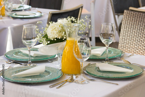 Small table nicely set for four people with orange juice jar in the middle at ceremony event. Nice restaurant, celebration setting concept