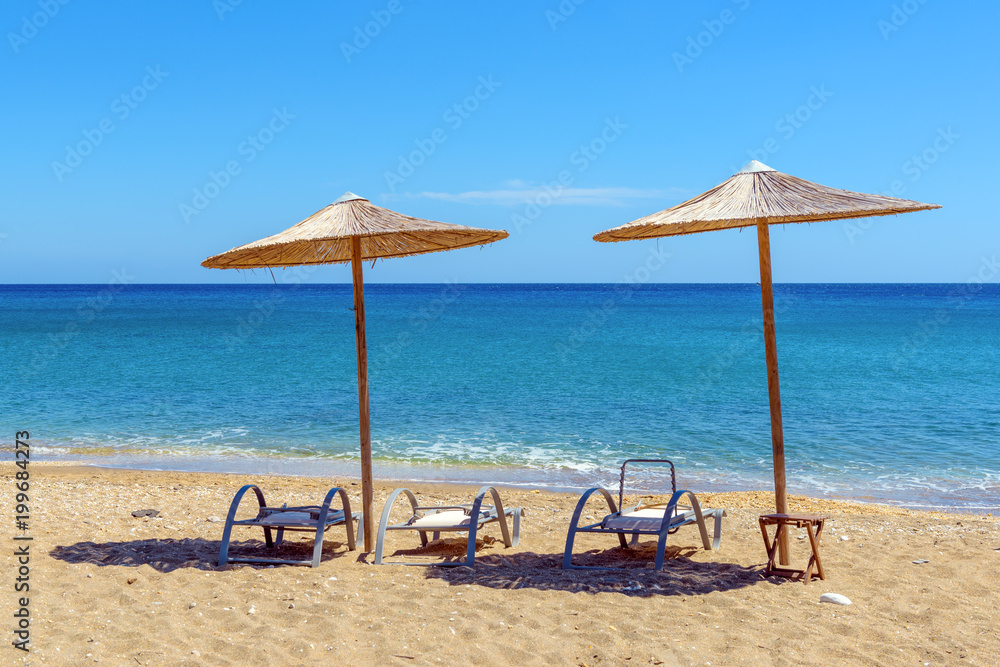 Sunbeds with umbrellas on Paleochori beach in sunny day on Milos island. Cyclades, Greece.