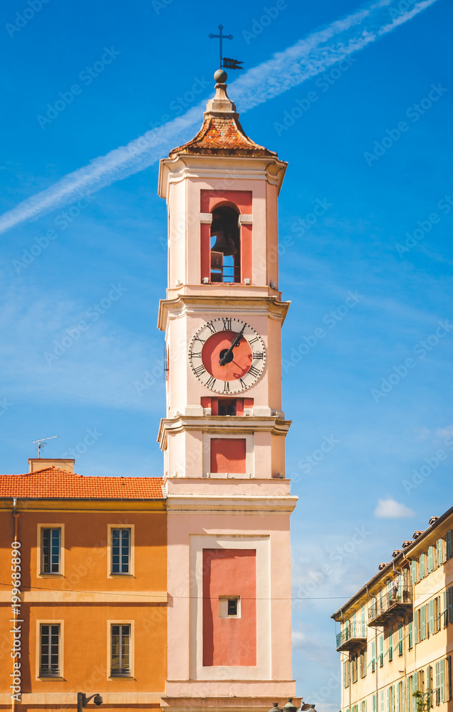 Colourful red and pink bell tower with clock against bright blue sky in Nice, Cote d'Azur, France