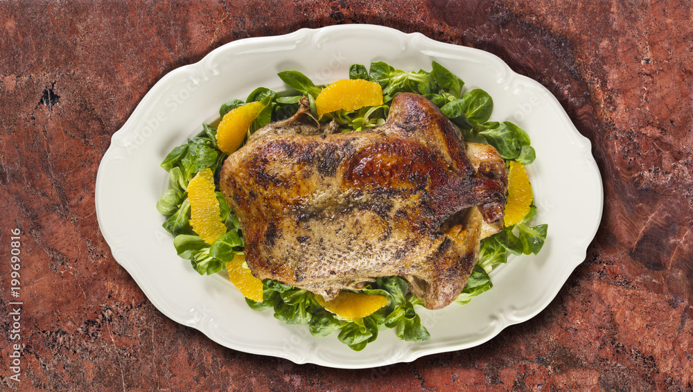 Baked duck in oranges and field salad or lamb's lettuce  on white plate on granite counter top.