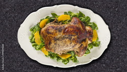 Baked duck in oranges and field salad or lamb's lettuce on white plate on granite counter top.