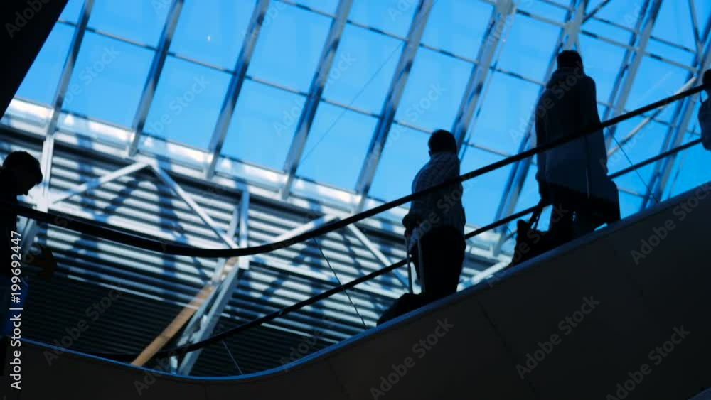 Commerce concept: customers figure elevated on the luxury department market centre. Male and female persons on the moving steps in modern hallway with beautiful view with blue sky from the ceiling Commerce concept: customers figure elevated on the luxury department market centre. Male and female persons on the moving steps in modern hallway with beautiful view with blue sky from the ceiling