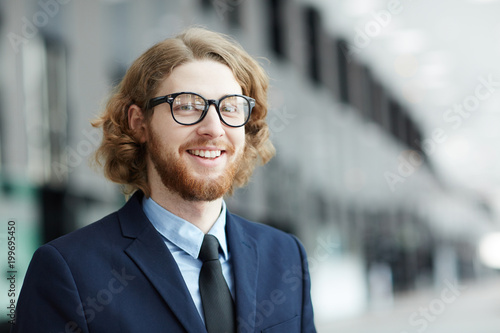 Young smiling bearded businessman in formalwear looking at camera inside modern building