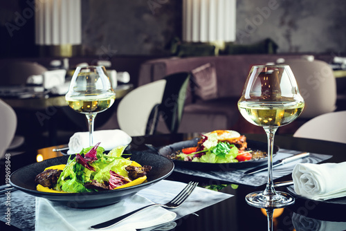 Romantic dinner at a restaurant. Appetizing dishes with meat and lettuce leaves and glasses with wine