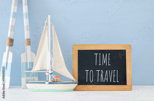 nautical concept with white decorative wooden oars and boat next to blackboard over blue background.