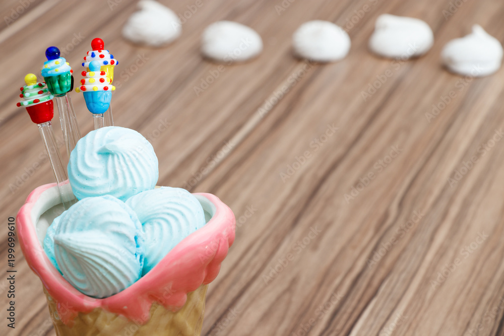 blue meringue in the pink cone with cupcakes on wood background and white meringues