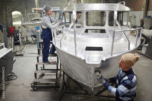 Modern shipbuilding engineers working over new boat in production factory photo