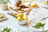 Boiled potatoes in porcelain bowl, plates with vegetable salad and other healthy food on served festive table