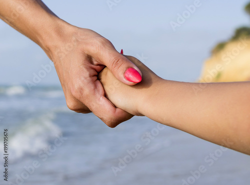 Mother and young son holding hands on sunny tropical beach, travel concept. © Evgen