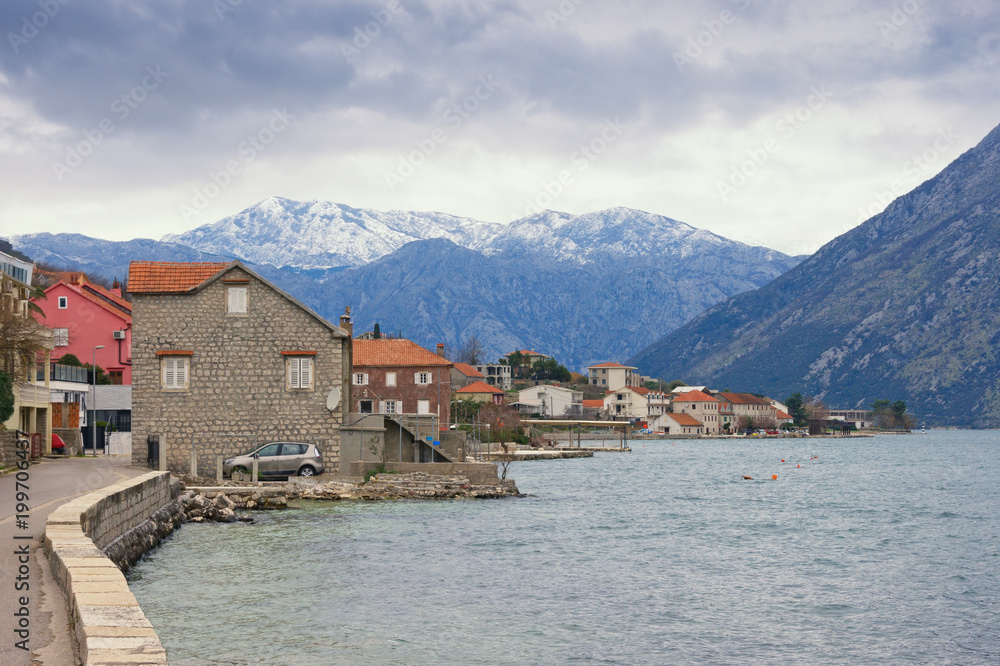Small Mediterranean town near snow-capped mountains on cloudy day. Montenegro,  Bay of Kotor (Adriatic Sea), Prcanj