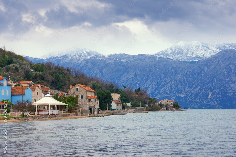 Cloudy landscape with snow-capped mountains and seaside town. Montenegro,  Bay of Kotor (Adriatic Sea), Prcanj