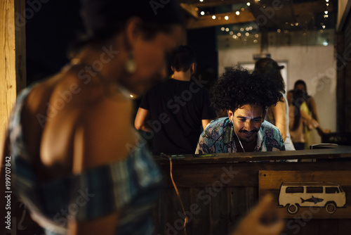 Indian ethnicity with afro hair DJ controlling equipment and people dancing in a tropical party in the caribbean in Santa Marta, Colombia photo